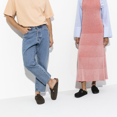 Man in jeans and woman in a pink dress both wearing Birkenstock Boston clogs in a minimalist setting.