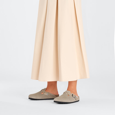 Woman wearing Birkenstock Boston clogs in taupe suede with braided straps, paired with a flowy beige skirt.