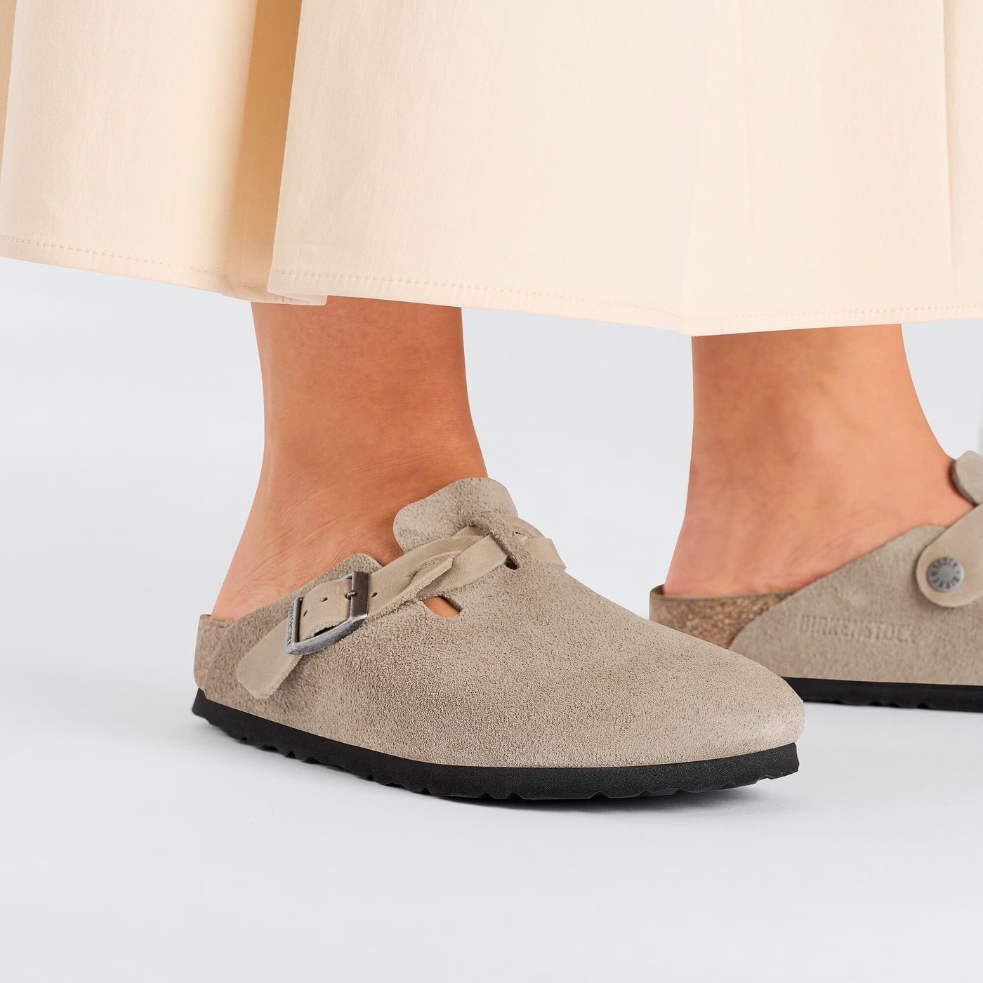 Close-up of Birkenstock Boston clogs in taupe suede with braided straps, paired with a flowy beige skirt.