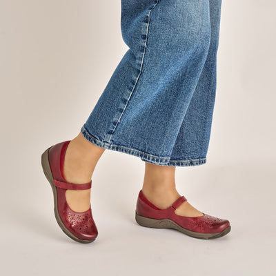 Women’s Dansko Stacy red leather Mary Jane featuring adjustable strap, cushioned EVA arch support, and slip-resistant outsole for stability.