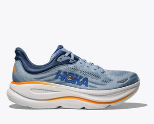 Side view of a light blue HOKA running shoe with breathable mesh uppers, navy blue and orange HOKA logo on the side, orange accents on the midsole, and a thick white cushioned sole for enhanced comfort and performance.