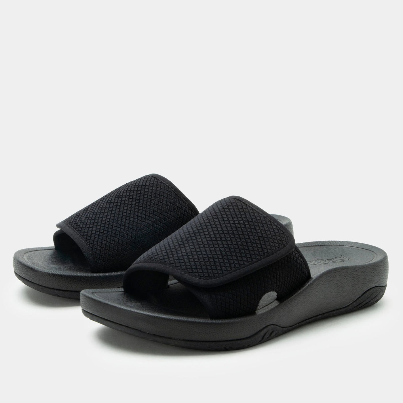 Pair of black open-toe slide sandals in a Raven colorway, featuring a wide adjustable strap, water-friendly design, and a built-in RecoverMe™ footbed for arch support and all-day comfort.