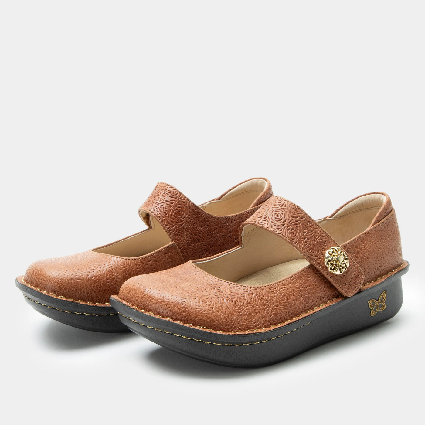 Pair of brown Mary Jane shoes with a laser-etched leather upper, adjustable hook-and-loop strap with a gold ornament, memory foam and cork footbed, and a classic rocker outsole for comfort and support.