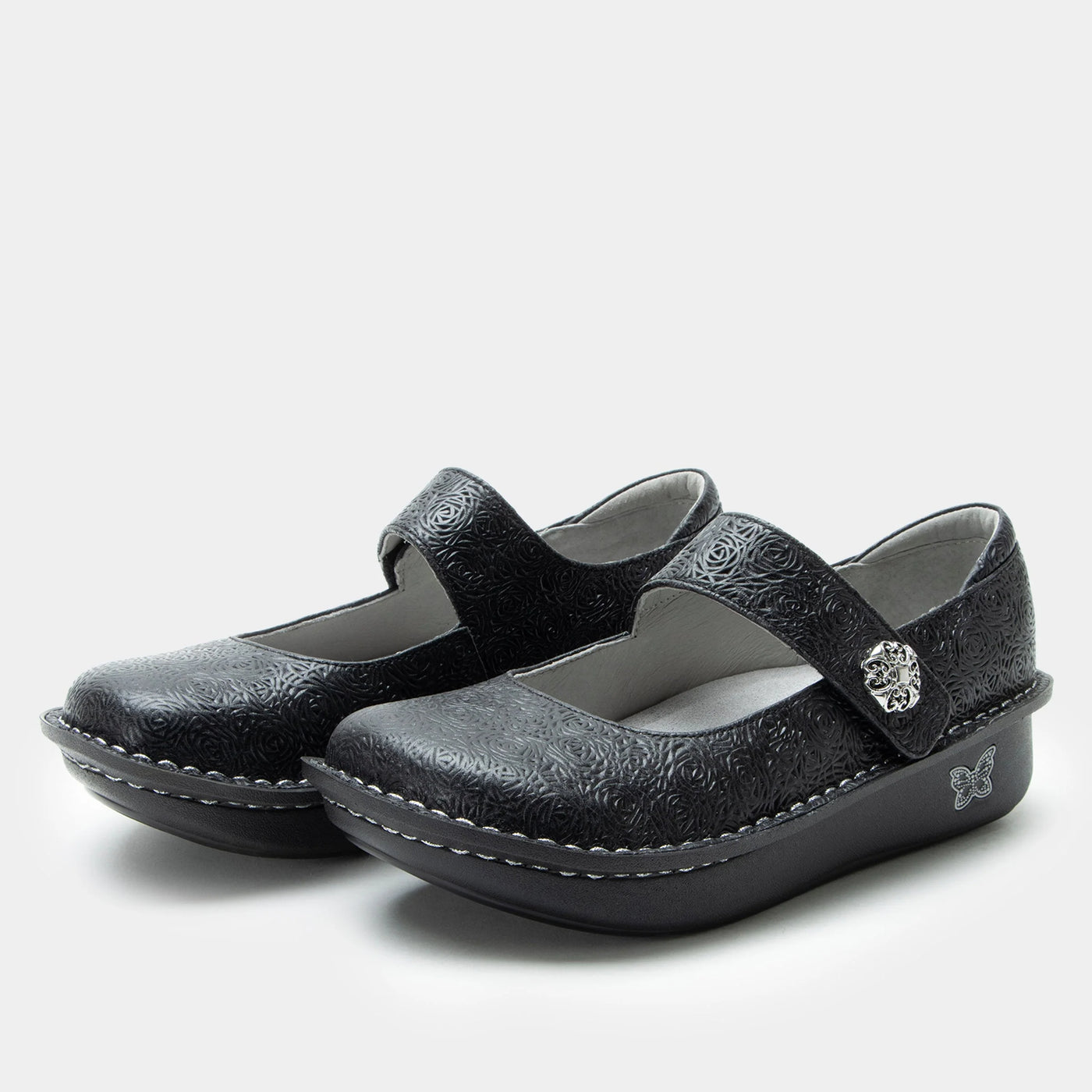 Pair of black Mary Jane shoes with a laser-etched leather upper, adjustable hook-and-loop strap with a silver ornament, memory foam and cork footbed, and a classic rocker outsole for comfort and support.