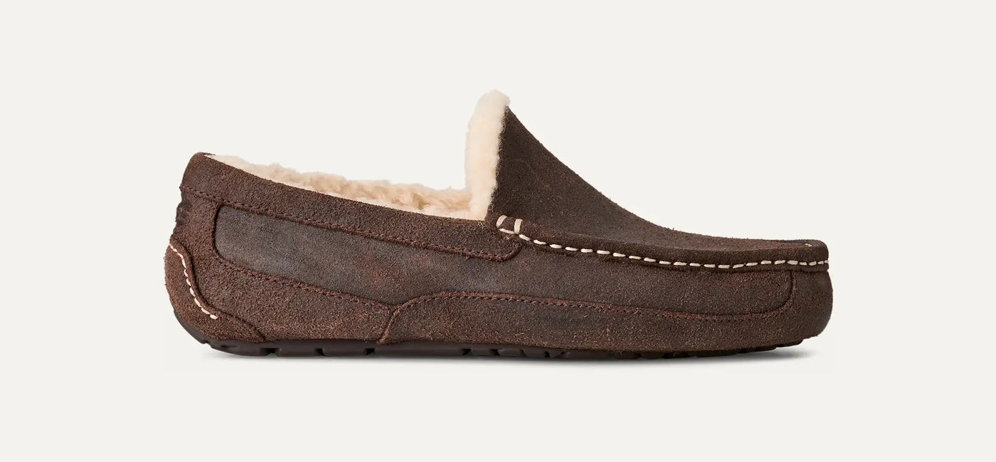 Brown suede UGG Ascot slip-on with moc-toe stitching, cozy wool-blend UGGplush lining, and treaded rubber outsole; side profile