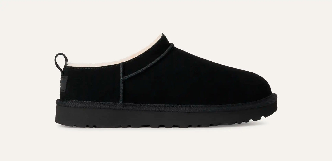 Black low-profile suede boot with plush sheepskin lining, rear pull tab, and lightweight sugarcane EVA sole; side view of UGG Classic Micro.