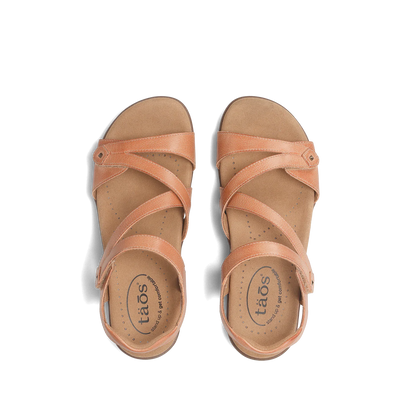 Top view of a pair of natural beige Taos sandals featuring crisscrossing adjustable straps and a cushioned, perforated footbed.